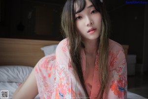 A woman in a pink kimono laying on a bed holding a fan.