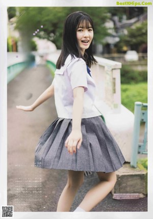 A woman in a school uniform standing in front of a fence.