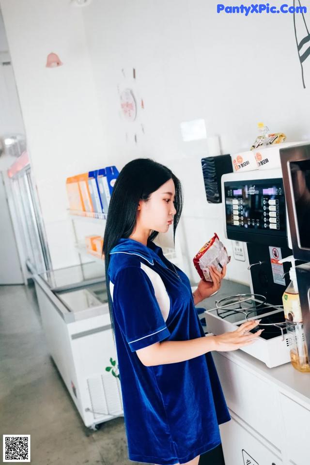 A woman in a blue dress standing in front of a microwave.