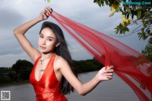 A woman in a red dress posing by the water.