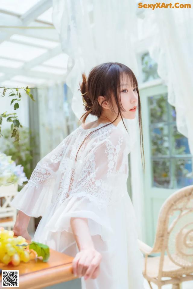 A woman in a white dress standing next to a table.