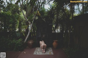 A naked woman laying on the ground in front of a stone wall.