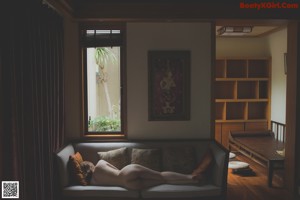 A naked woman laying on a wooden bench on a deck.