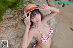 A woman in a bikini and a straw hat on the beach.