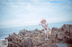 A woman with pink hair wearing a straw hat on the beach.