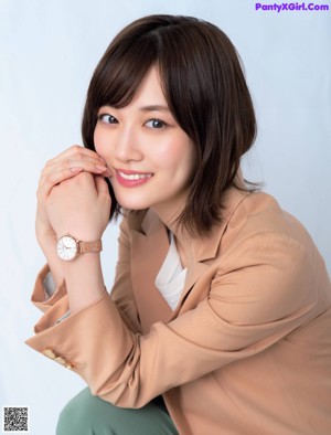 A woman leaning against a wooden wall with her hand on her chin.