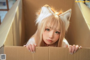 A naked woman sitting in a cardboard box with a cat tail.
