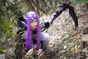 A woman with purple hair standing on a rock in the woods.