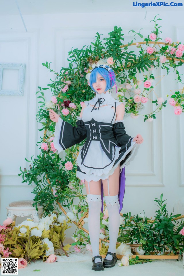 A woman dressed in a maid outfit standing in front of flowers.