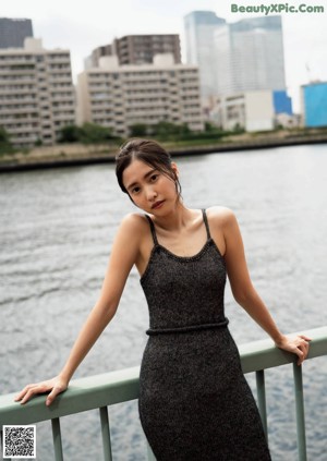 A woman with long brown hair standing in front of a bridge.