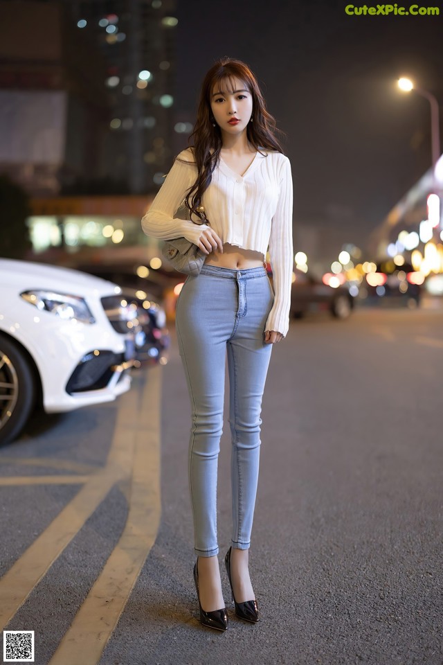 A woman standing in the middle of a parking lot at night.