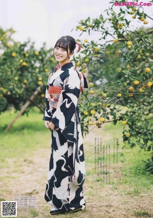 A woman in a kimono leaning against a yellow fence.