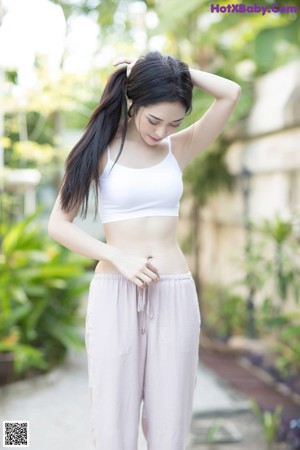 A woman in a white top and pink pants leaning against a wall.