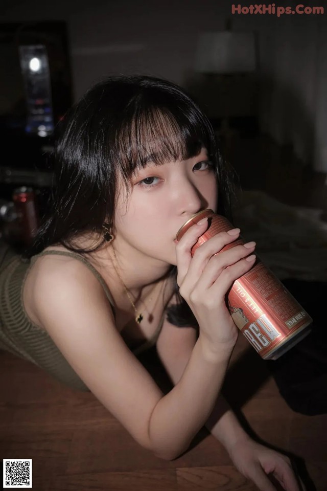 A woman laying on the floor drinking from a can.