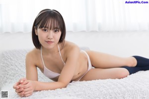 A woman in a white bikini sitting on a bed.