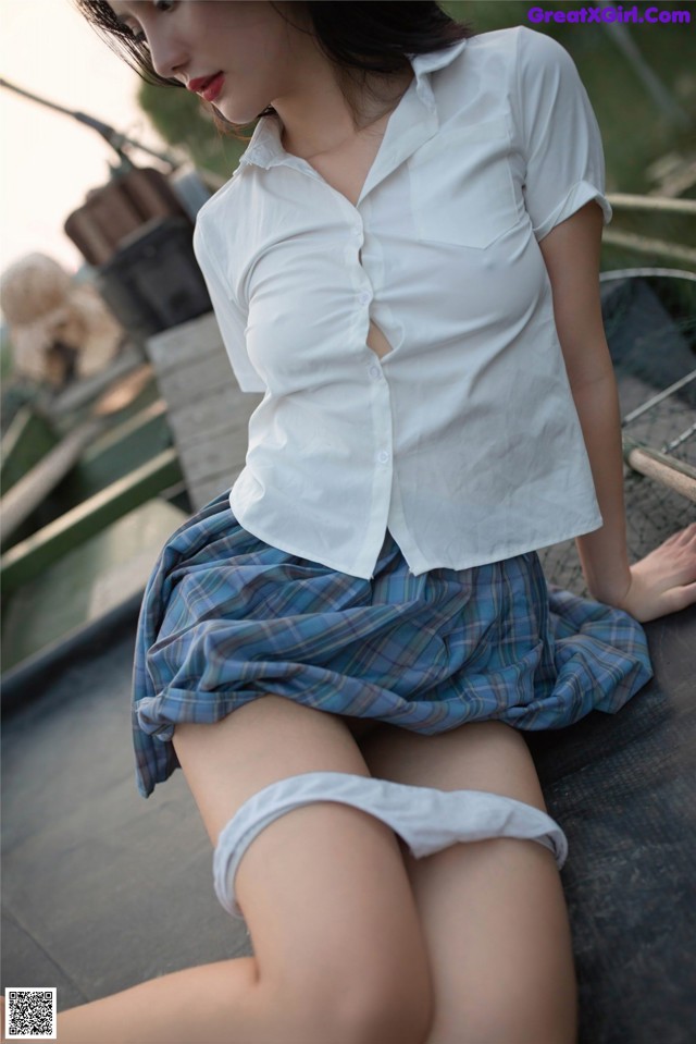 A woman in a white shirt and plaid skirt sitting on a bench.